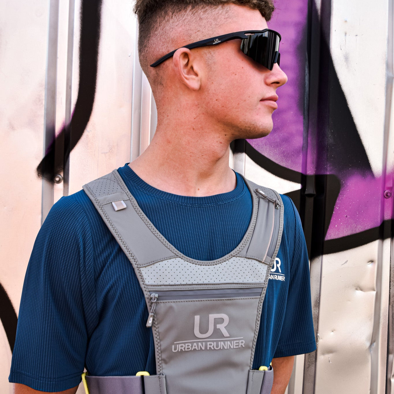 Man wearing a blue athletic shirt and gray Urban Runner vest against a colorful background
