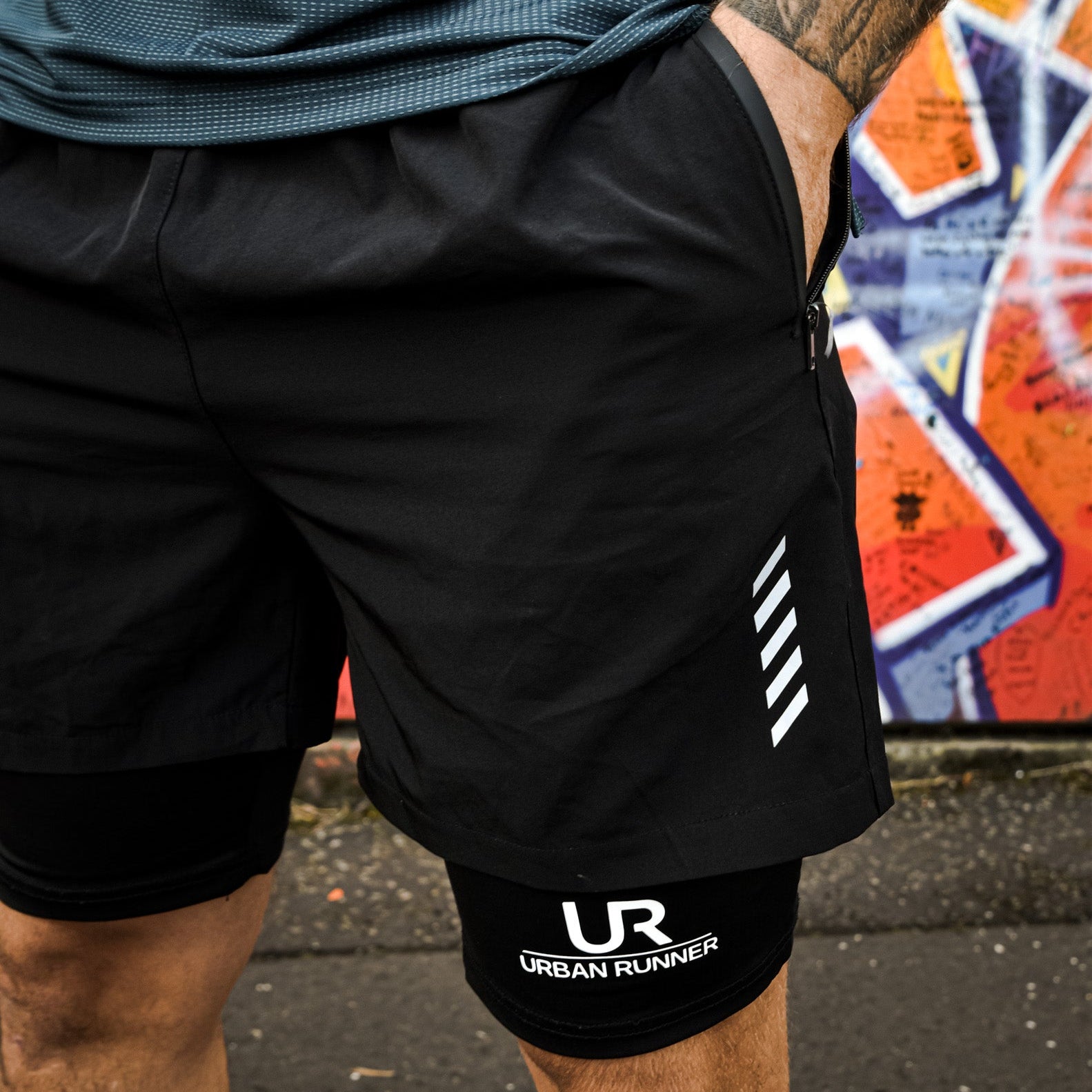 Person wearing black athletic shorts with 'Urban Runner' branding in front of a colorful mural.